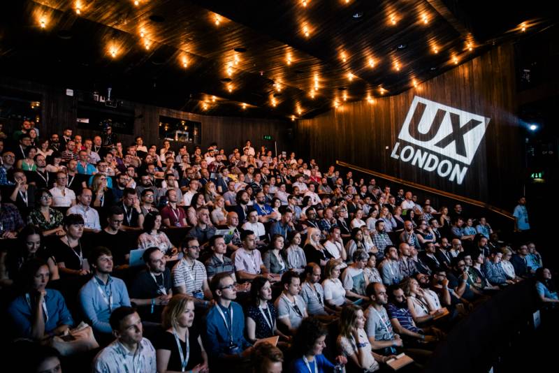 An ambiently lit view over the UX London conference hall. A UX London logo is projected on the wall.